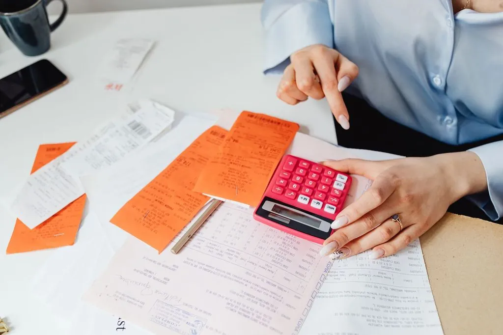 Manos con una calculadora sobre un escritorio lleno de recibos